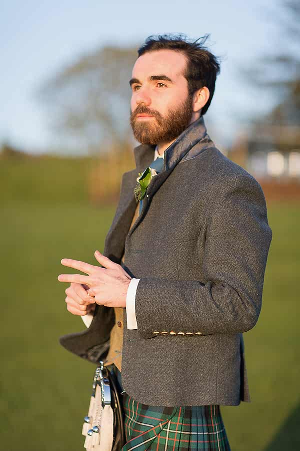 groom holding his ring on a finger looking away