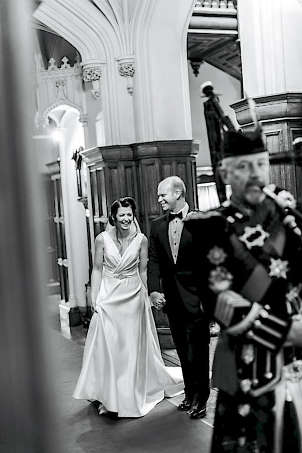 bride and groom laughing beeing leaded by scottish piper