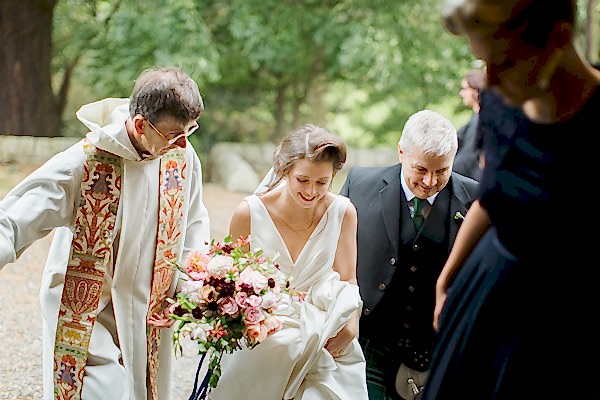 bride walking in to teh church with father and minister