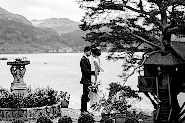 married couple embraced next to vintage fountian with tree house and loch goil in background