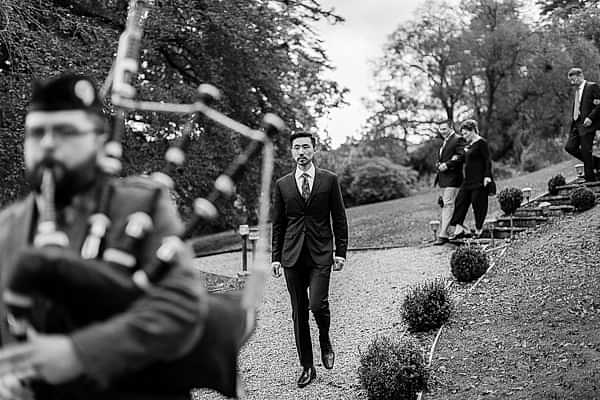 scottish piper and groom with guests walking to ceremony in scotland