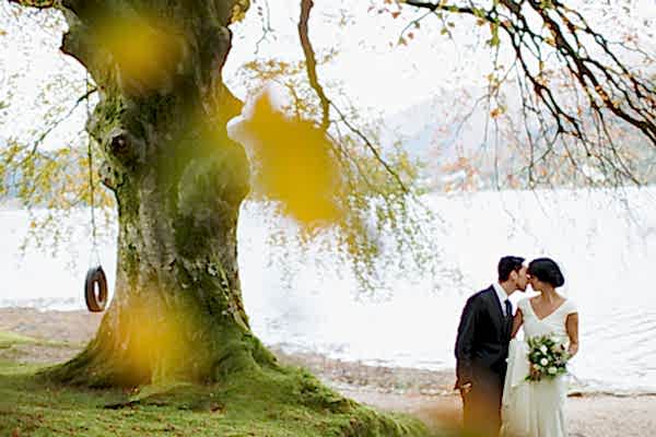 bride and groom kissing with large tree and loch in the background