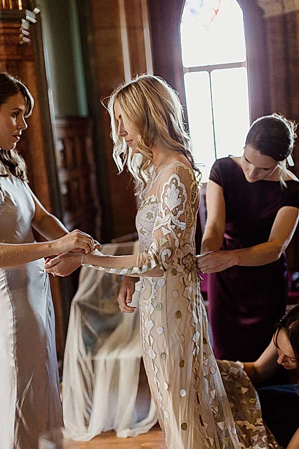 bride putting dress on bridesmates helping